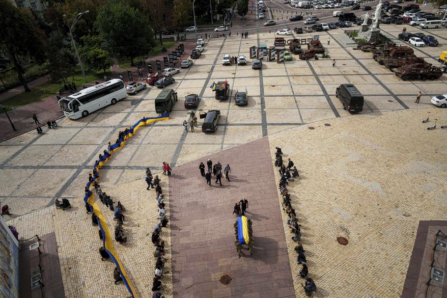 People kneel down, as honor guards carry the coffin of Artem Antonenko, a Ukrainian serviceman, during his funeral ceremony in the center of Kyiv, Ukraine, Friday, Sept. 19, 2025. (AP Photo/Evgeniy Maloletka)