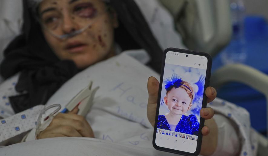Amani Bazzi, who was injured Sunday in the town of Bint Jbeil, shows a portrait of one her three kids who were killed after an Israeli drone strike hit her family car, as she lies in Tibnin hospital, southern Lebanon, Monday, Sept. 22, 2025. (AP Photo/Mohammed Zaatari)