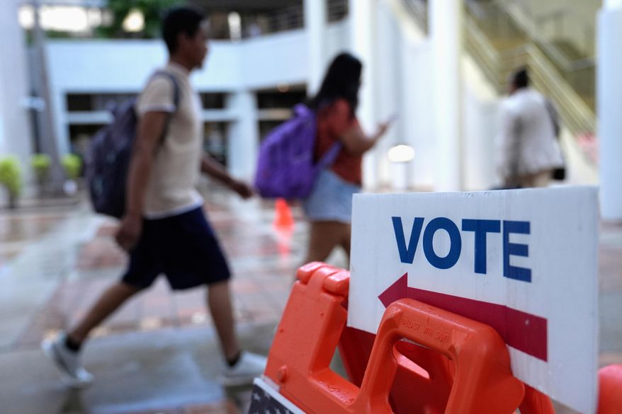 FILE - People walk past a "vote" sign on the first day of early voting in the general election in Miami, on Oct. 21, 2024. (AP Photo/Lynne Sladky, File)