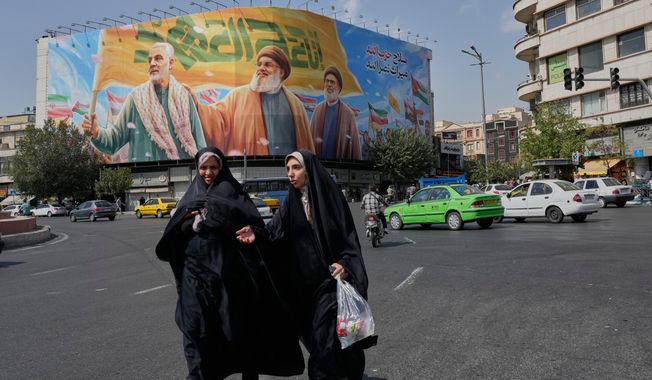 Two women walk past a huge banner showing the late commander of the Iran's Revolutionary Guard expeditionary Quds Force, Gen. Qassem Soleimani, who was killed in a U.S. drone attack in 2020, and two late Hezbollah leaders Hassan Nasrallah, center, and Hashem Safieddine, who were killed in Israeli airstrikes in 2024, at the Enqelab-e-Eslami (Islamic Revolution) square, in Tehran, Iran, Saturday, Sept. 27, 2025. (AP Photo/Vahid Salemi)