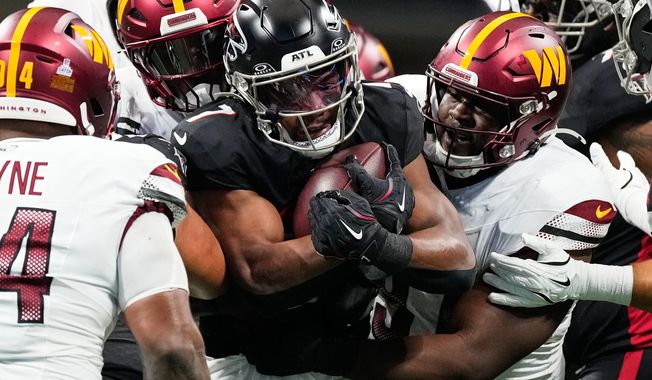 Atlanta Falcons running back Bijan Robinson, center, is tackled by Washington Commanders defenders during the first half of an NFL football game, Sunday, Sept. 28, 2025, in Atlanta. (AP Photo/Brynn Anderson)