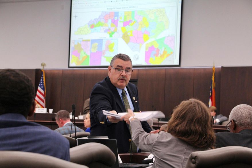 FILE - A sergeant-at-arms in the North Carolina state Senate passes out copies of a map proposal for new state Senate districts during a committee hearing at the Legislative Office Building in Raleigh, N.C., Oct. 19, 2023. (AP Photo/Hannah Schoenbaum, File)