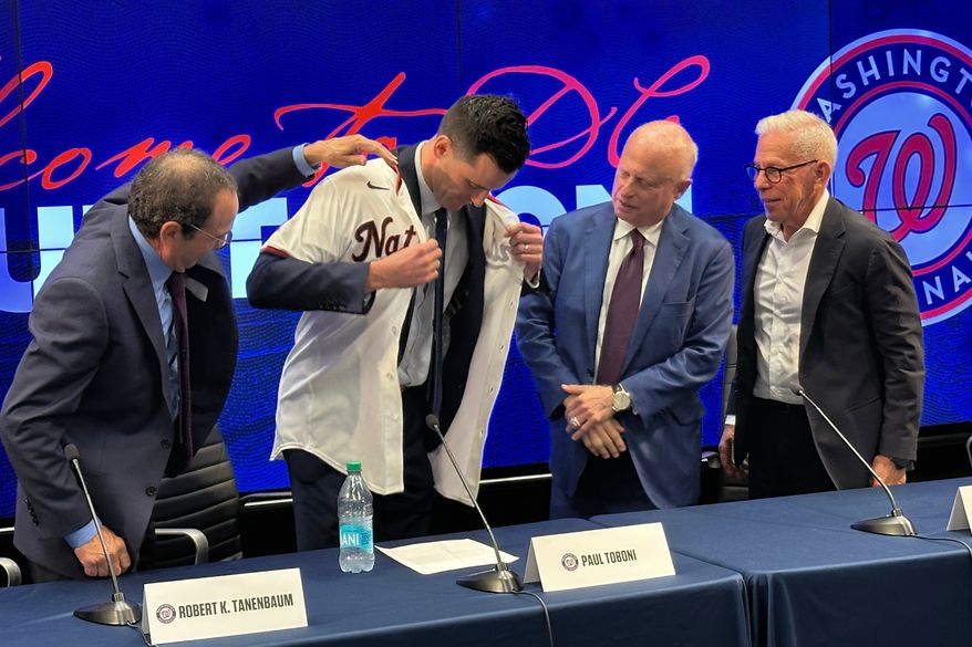 Washington Nationals new president of baseball operations Paul Toboni, second from left, puts on a team jersey as club owners Robert Tanenbaum, left, Mark Lerner, center, and Edward Cohen, right, look on during a news conference at Nationals Park in Washington, Wednesday, Oct. 1, 2025. (AP Photo/Howard Fendrich)