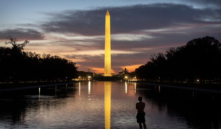 A visitor stands along the reflecting pool near the Washington Monument at dawn on Wednesday, Oct. 1, 2025, in Washington. (AP Photo/Mark Schiefelbein)