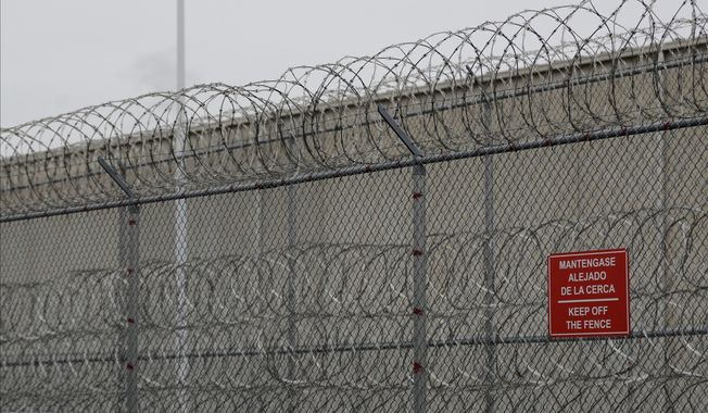 FILE - Barbed wire fencing is shown behind a sign in English and Spanish in a recreation yard used by detainees during a media tour of the U.S. Immigration and Customs Enforcement detention center, Dec. 16, 2019, in Tacoma, Wash. (AP Photo/Ted S. Warren, file)