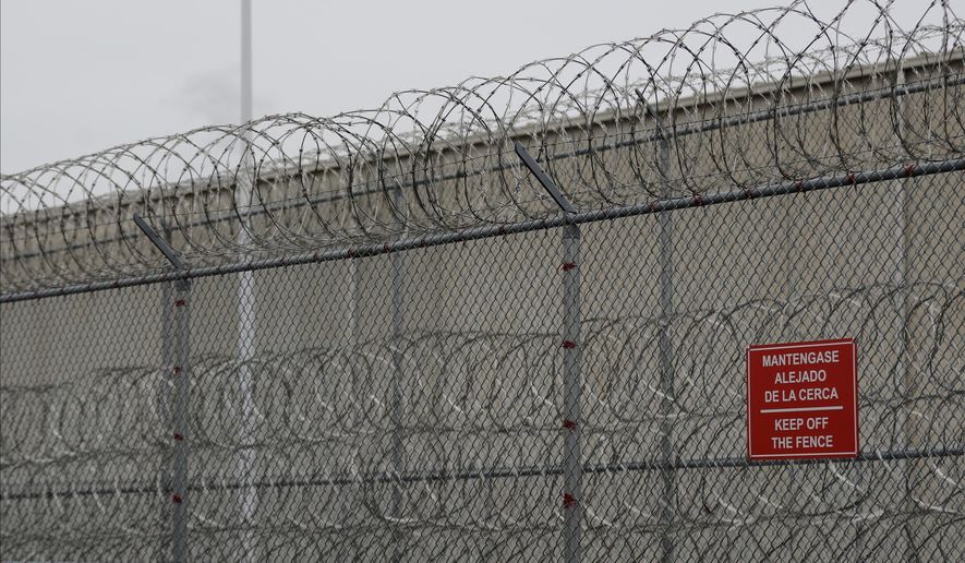 FILE - Barbed wire fencing is shown behind a sign in English and Spanish in a recreation yard used by detainees during a media tour of the U.S. Immigration and Customs Enforcement detention center, Dec. 16, 2019, in Tacoma, Wash. (AP Photo/Ted S. Warren, file)