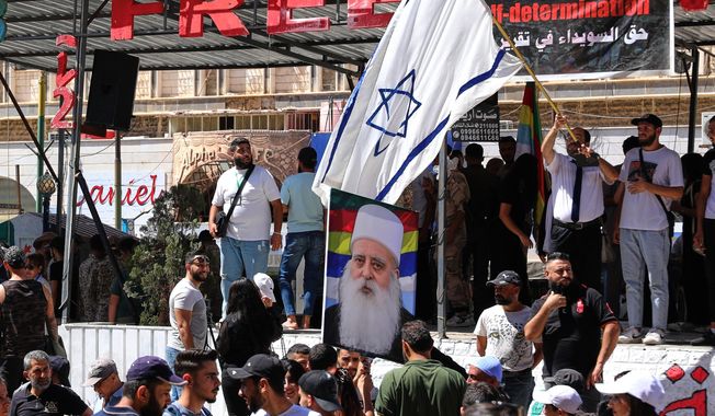 A man waves an Israeli flag over a picture of Sheikh Mowafak Tarif, the spiritual leader of the Druze in Israel, during a weekly rally in Sweida, southern Syria, on Sept. 20, 2025. (AP Photo/Fahd Kiwan)