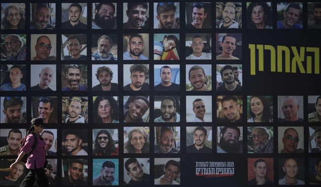 A woman walks past a banner with photographs of hostages who were kidnapped and held by Hamas in the Gaza Strip, in Jerusalem, Tuesday, Oct. 7, 2025, on the second anniversary of Hamas' cross-border attack on Israel on Oct. 7, 2023, which sparked the ongoing war in Gaza. (AP Photo/Leo Correa)