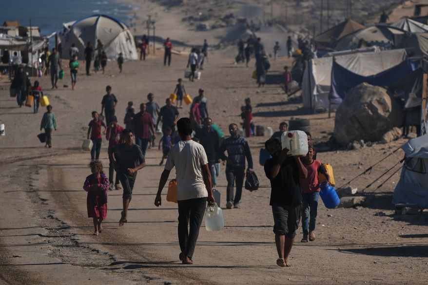 Palestinians carry plastic bottles with water in an area of a makeshift tent camp for displaced people along the shore of Nuseirat, in the central Gaza Strip, Wednesday, Oct. 8, 2025. (AP Photo/Abdel Kareem Hana)