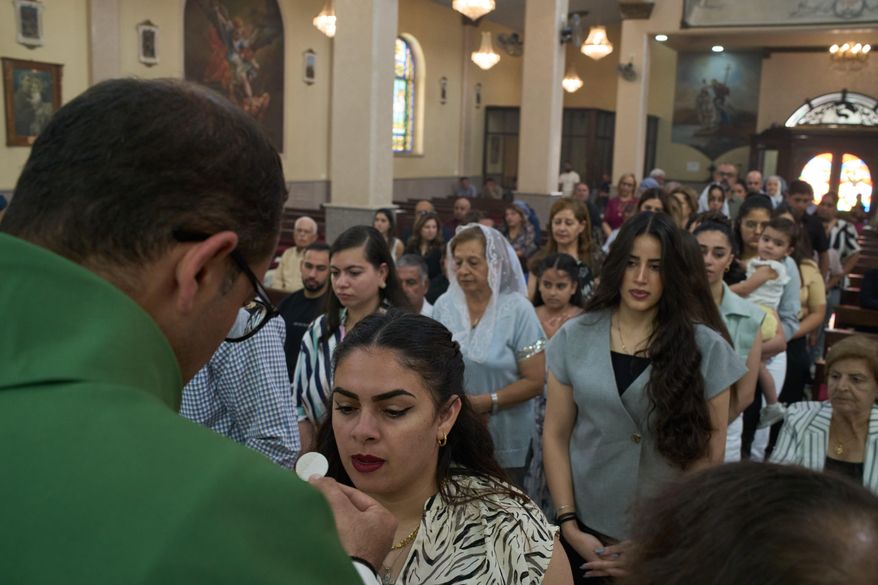 Catholic parish priest Bashar Fawadleh offers a communion wafer to a faithful during Mass at Christ the Redeemer Church in the West Bank village of Taybeh, Sept. 28, 2025. (AP Photo/Leo Correa)
