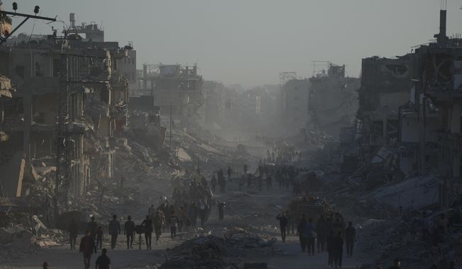 Displaced Palestinians carry their belongings as they walk along the heavily damaged Al-Jalaa Street in Gaza City, Saturday, Oct. 11, 2025, after Israel and Hamas agreed to a pause in their war and the release of the remaining hostages. (AP Photo/Abdel Kareem Hana)