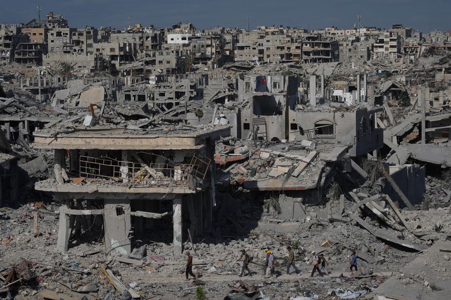 Displaced Palestinians walk through an area surrounded by destroyed buildings in Khan Younis, in the southern Gaza Strip, Saturday, Oct. 11, 2025, after Israel and Hamas agreed to a pause in their war and the release of the remaining hostages. (AP Photo/Jehad Alshrafi)