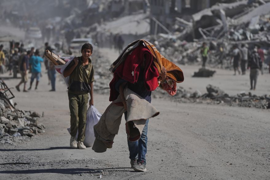Displaced Palestinians carry their belongings as they walk along the heavily damaged Al-Jalaa Street in Gaza City, Saturday, Oct. 11, 2025, after Israel and Hamas agreed to a pause in their war and the release of the remaining hostages. (AP Photo/Abdel Kareem Hana)