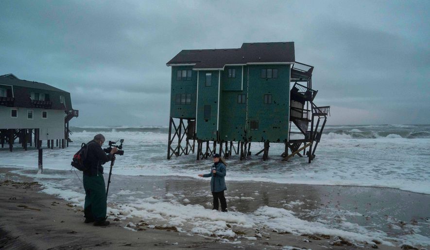 A Fox Weather reporter films in front of a house at risk of collapse in the midst of a storm, Sunday, Oct. 12, 2025, in Buxton, N.C. (AP Photo/Allison Joyce)