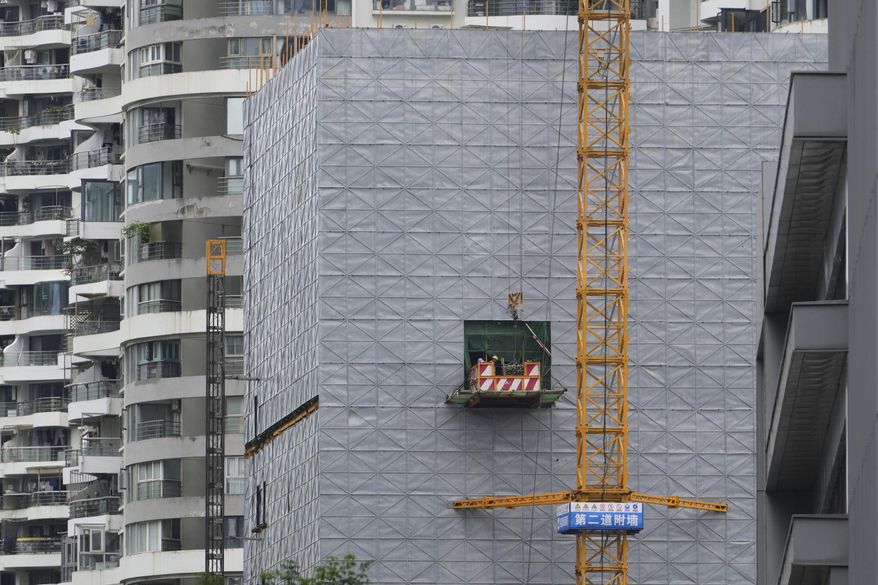 Workers on a platform transfer materials to a building under construction near residential buildings, at the Shenzhen Bay commercial district, in Shenzhen, China's Guangdong province, Friday, Sept. 19, 2025. (AP Photo/Andy Wong)