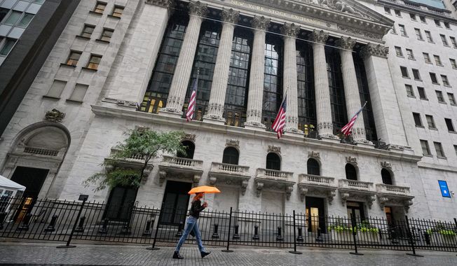 A woman with an umbrella passes the New York Stock Exchange, Monday, Oct. 13, 2025. (AP Photo/Richard Drew)