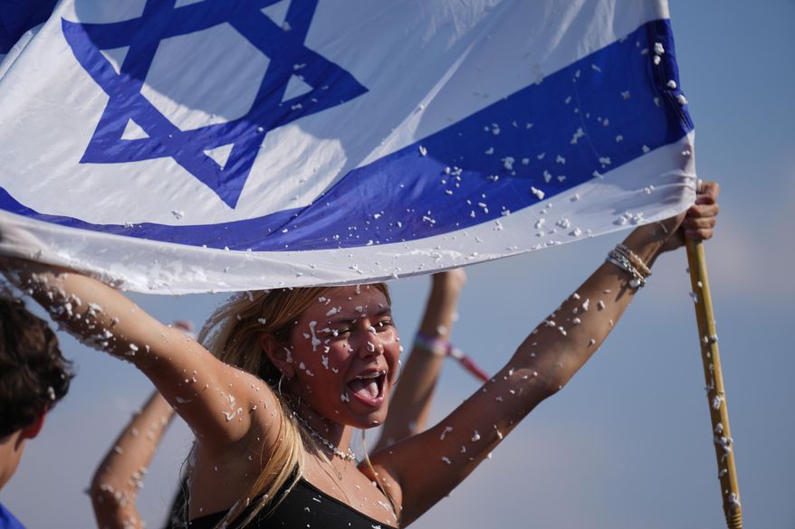 People hold Israeli flag and spray foam in celebration after the arrival of freed hostages at Beilinson Hospital in Petah Tikva, Israel, following their release from Hamas captivity in the Gaza Strip, Monday, Oct. 13, 2025. (AP Photo/Ariel Schalit)