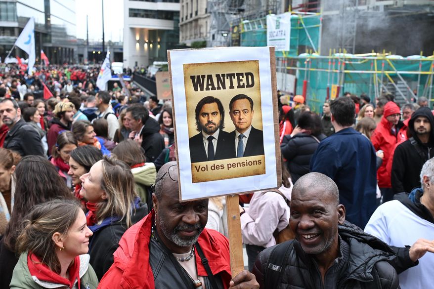 Two men hold a sign with a photo of Belgium's Prime Minister Bart De Wever, which reads 'Pension Theft', during a demonstration and general strike in Brussels, Tuesday, Oct. 14, 2025. (AP Photo/Harry Nakos)
