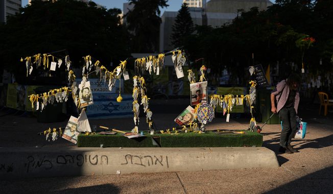 A man walks past photographs of Israeli hostages who were held by Hamas in the Gaza Strip, at the plaza known as Hostages Square, in Tel Aviv, Israel, Tuesday, Oct. 14, 2025. (AP Photo/Francisco Seco)