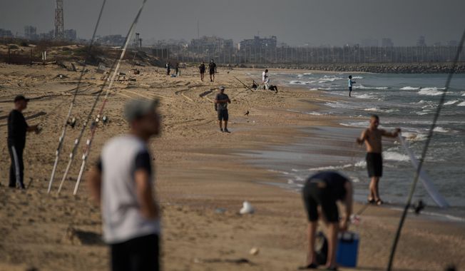 Backdropped by buildings destroyed during Israeli ground and air operations in the northern Gaza Strip, people walk and fish at Zikim Beach, near Ashkelon, in southern Israel, Friday, Oct. 17, 2025. (AP Photo/Leo Correa)