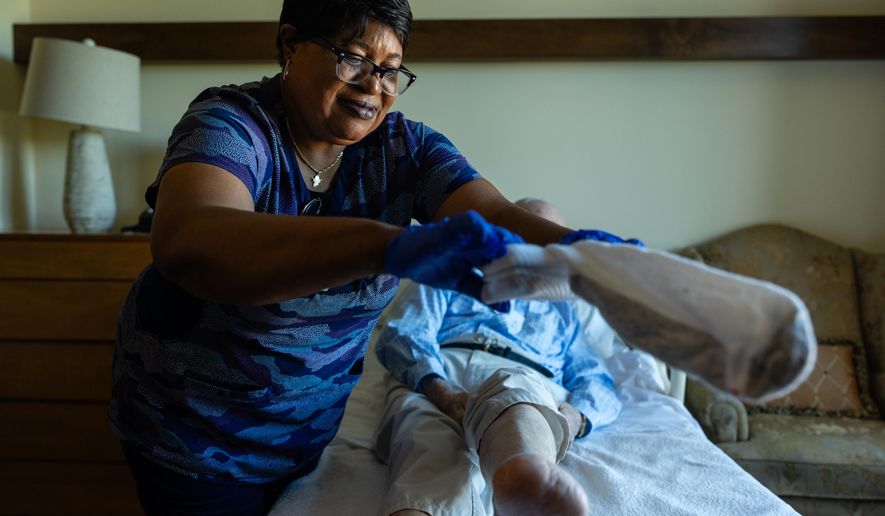 Jackie Conteh, an advanced care partner originally from Sierra Leone, helps Donald Goodness, 92, put on fresh socks in his apartment at Goodwin House Alexandria, Thursday, Oct. 16, 2025, in Alexandria, Va. (AP Photo/Eric Lee)