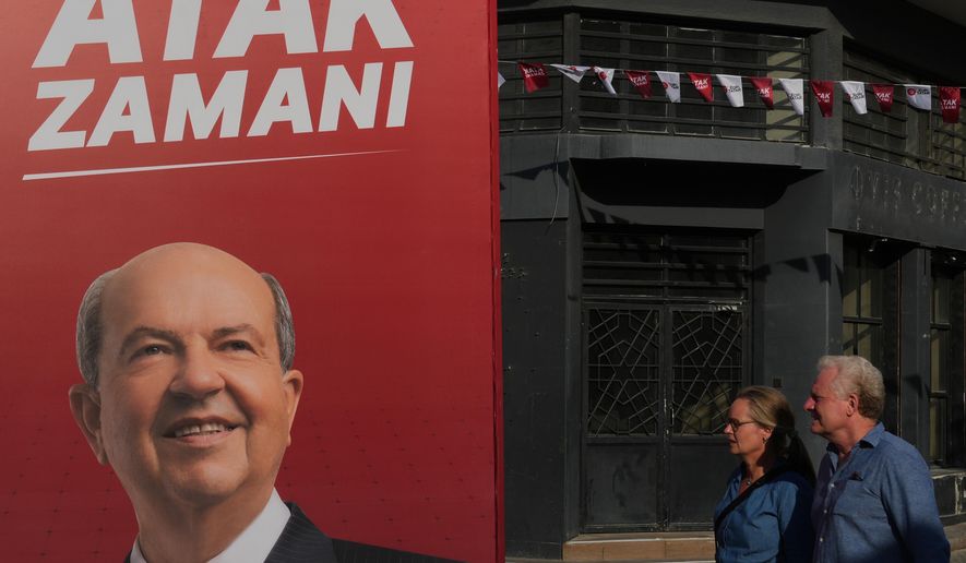 A couple walk past a campaign poster of Turkish Cypriot leader and candidate Ersin Tatar ahead of the Turkish Cypriot elections in the Turkish occupied northern part of divided Nicosia, Cyprus, Friday, Oct. 17, 2025. (AP Photo/Petros Karadjias)