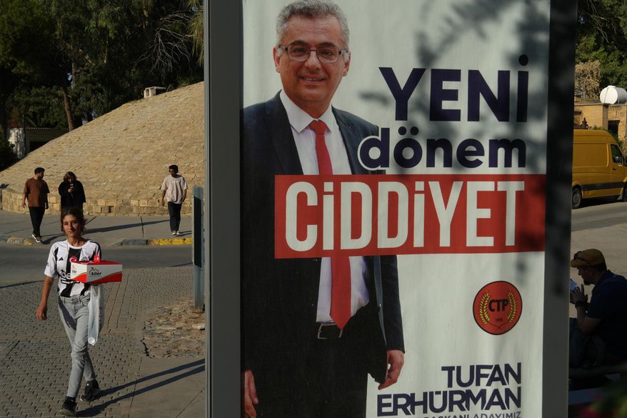 People walk past a campaign poster of Turkish Cypriot candidate Tufan Erhurman ahead of the Turkish Cypriot elections in the Turkish occupied northern part of divided Nicosia, Cyprus, Friday, Oct. 17, 2025. (AP Photo/Petros Karadjias)
