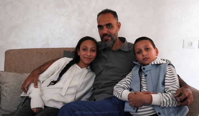 Palestinian medical technician Mohammed Abu Moussa, 45, who was released from Israeli detention after 20 months, poses for a photo with his children, Jourie and Hamid, in Deir al-Balah, Gaza, Saturday, Oct, 18, 2025. (AP Photo/Abdel Kareem Hana)