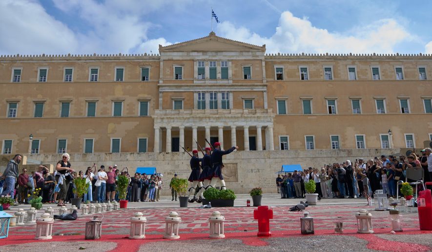 Tourists watch the changing of the guard at the Tomb of the Unknown Soldier in front of the Greek parliament, in Athens, Tuesday, Oct. 21, 2025, as lawmakers debate regulations to protect the monument, recently the focus of protests by relatives of victims of Greece's deadliest train crash. (AP Photo/Petros Giannakouris)