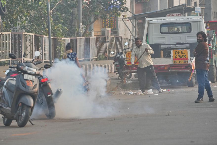 A municipal worker sweeps as a person burns firecrackers amidst morning smog in New Delhi, India, Tuesday, Oct. 21, 2025. (AP Photo/Manish Swarup)