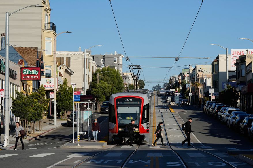People cross Taraval Street after exiting a MUNI train in the Sunset District, Friday, Oct. 17, 2025, in San Francisco. (AP Photo/Godofredo A. Vásquez)