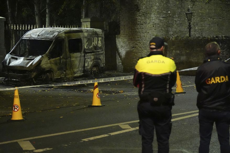 Garda Siochana police officers stand at the scene of a burned out police vehicle, near the Citywest Hotel, where disturbances have flared outside the Dublin hotel which used to house asylum seekers, Wednesday, Oct. 22, 2025. (Niall Carson/PA via AP)