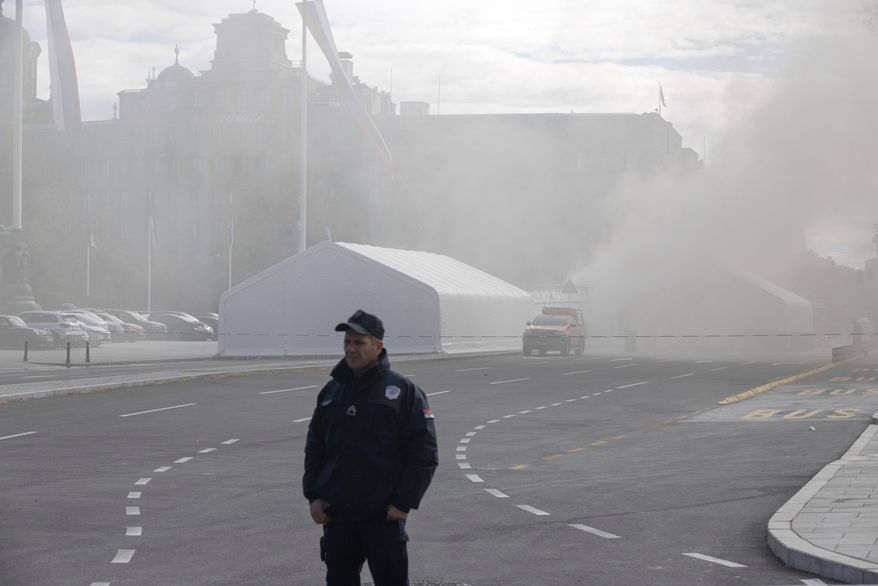 A policeman stands guard as a fire is localized inside the government supporters' camp outside the Serbian parliament in Belgrade, Serbia, Wednesday, Oct. 22, 2025. (AP Photo/Marko Drobnjakovic)