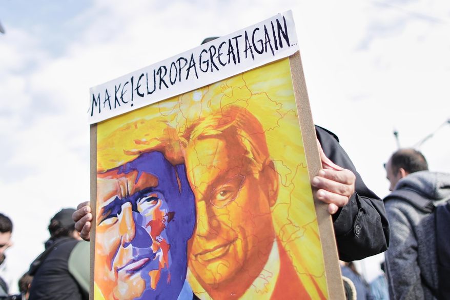 A pro-government demonstrator holds a sign with drawings of U.S. President Donald Trump and Hungarian Prime Minister Viktor Orban during celebrations marking the 69th anniversary of the outbreak of Hungary's 1956 revolution against communist rule and the Soviet Union, in Budapest, Hungary, Thursday, Oct. 23, 2025. (AP Photo/Rudolf Karancsi)