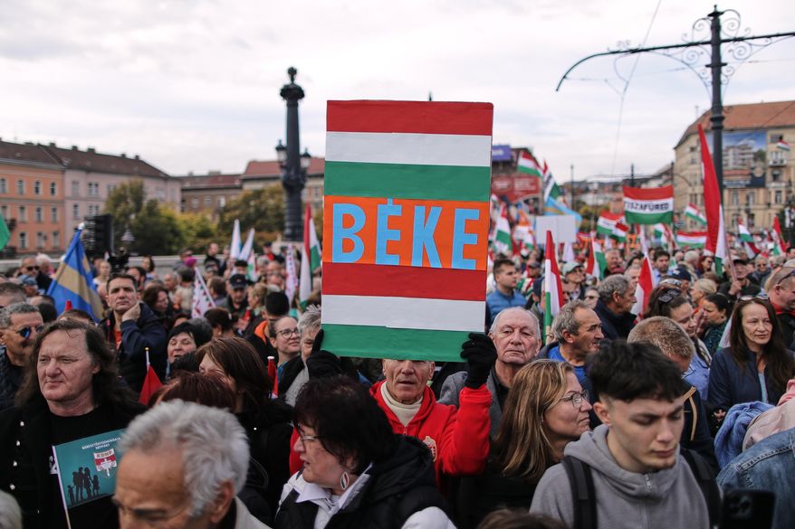 A pro-government demonstrator holds a sign reading "Peace" in Hungarian during celebrations marking the 69th anniversary of the outbreak of Hungary's 1956 revolution against communist rule and the Soviet Union, in Budapest, Hungary, Thursday, Oct. 23, 2025. (AP Photo/Rudolf Karancsi)