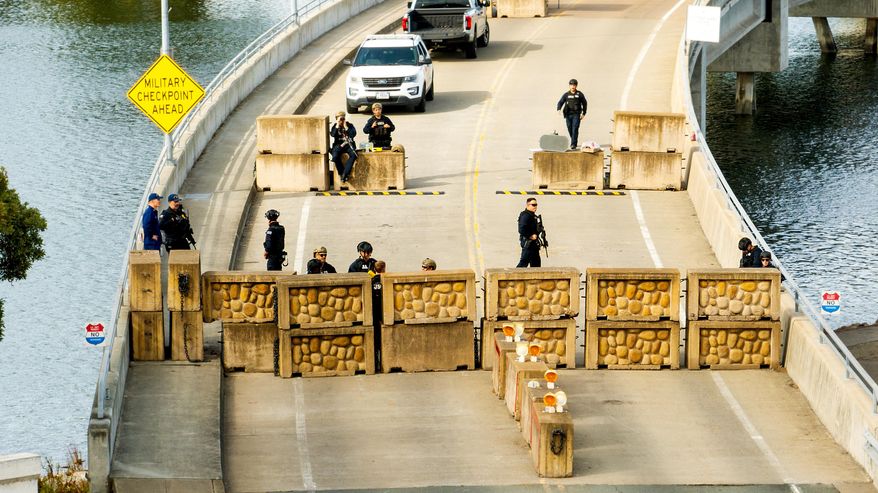 Coast Guardsmen stand watch behind a barrier at Coast Guard Base Alameda on Friday, Oct. 24, 2025, in Oakland, Calif. The barrier was erected earlier in the day after law enforcement officers fired on a vehicle as it backed towards them. (AP Photo/Noah Berger)
