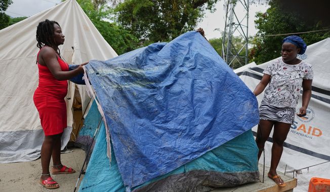 People place plastic tarps over their tents ahead of expected rain at a shelter for families displaced by gang violence in Port-au-Prince, Haiti, Thursday, Oct. 23, 2025. (AP Photo/Odelyn Joseph)