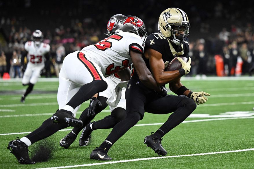 New Orleans Saints wide receiver Chris Olave (12) is stopped by Tampa Bay Buccaneers cornerback Jamel Dean (35) and safety Antoine Winfield Jr. during the second half of an NFL football game Sunday, Oct. 26, 2025, in New Orleans. (AP Photo/Ella Hall)