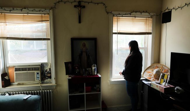A parishioner of the Shrine of the Sacred Heart, whose husband was detained by immigration agents, looks out her home's window as she poses for a portrait in Washington, Friday, Oct. 10, 2025. (AP Photo/Luis Andres Henao)