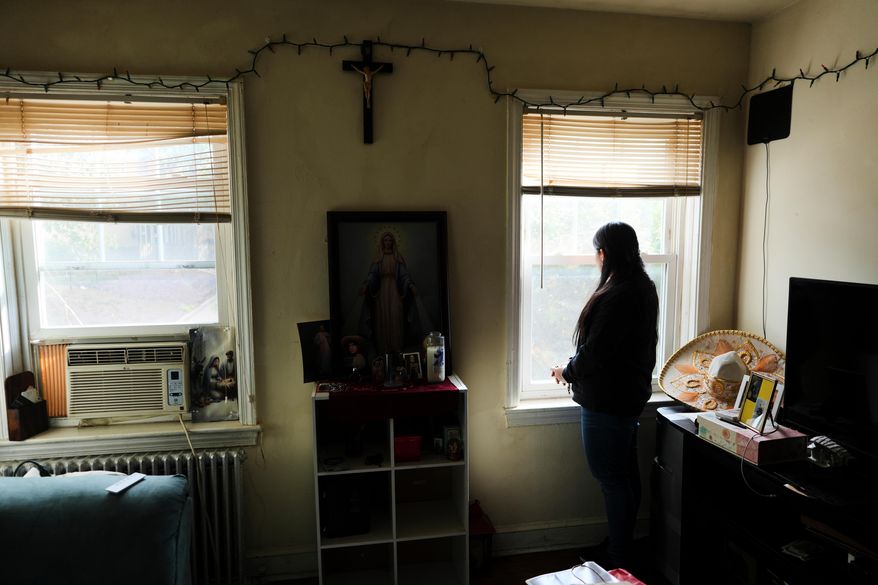 A parishioner of the Shrine of the Sacred Heart, whose husband was detained by immigration agents, looks out her home's window as she poses for a portrait in Washington, Friday, Oct. 10, 2025. (AP Photo/Luis Andres Henao)