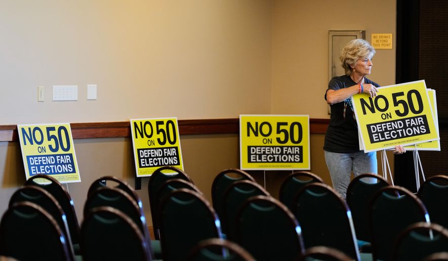 Brenda Haynes places signs throughout a conference room before a No on Prop 50 rally in Redding, Calif., Tuesday, Oct. 21, 2025. (AP Photo/Godofredo A. Vásquez)
