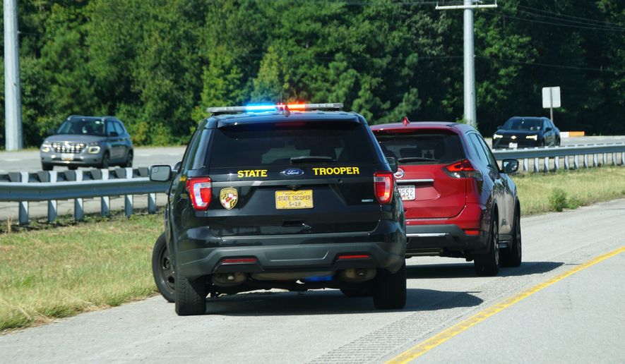 A Maryland State Trooper's patrol car with activated lights pulled over a red Nissan SUV on the shoulder of a highway. File photo credit: Khairil Azhar Junos via Shutterstock.