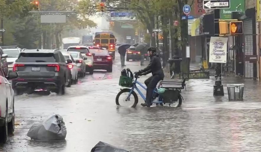 A cyclist rides through floodwaters during a rainstorm in New York, Thursday, Oct. 30, 2025. (AP Photo/David Martin)