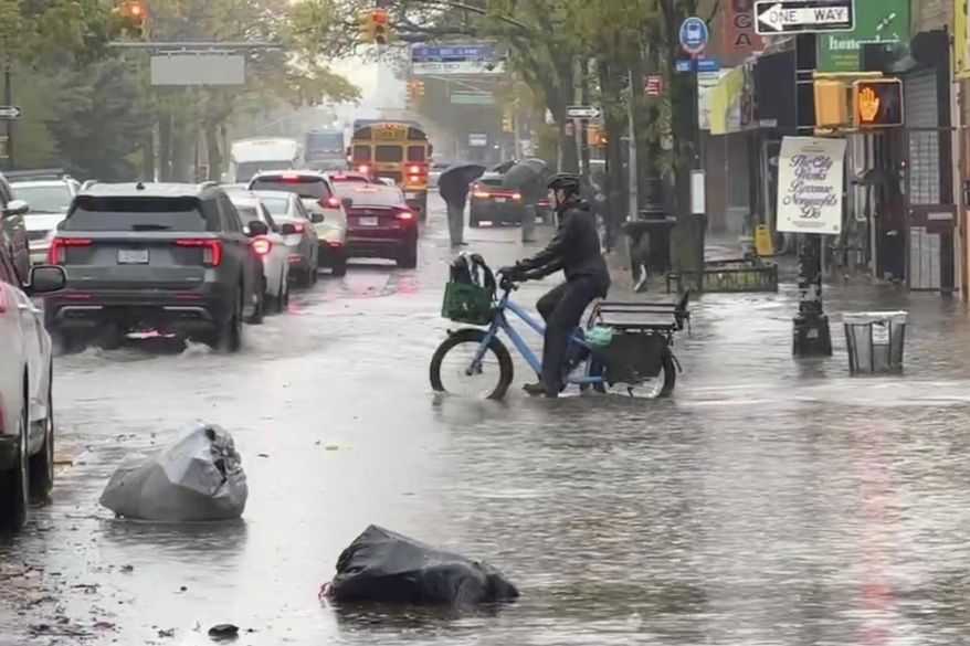 A cyclist rides through floodwaters during a rainstorm in New York, Thursday, Oct. 30, 2025. (AP Photo/David Martin)