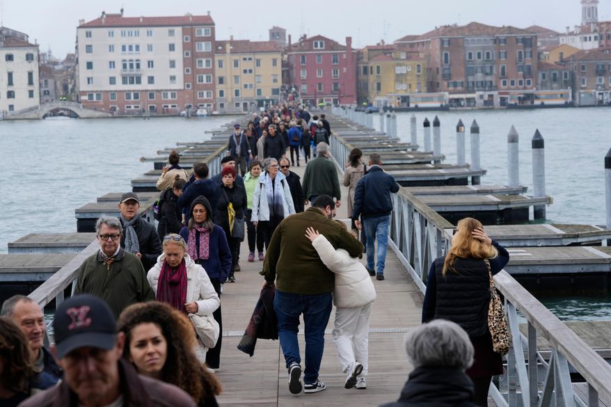 Mourners walk on the 'Votif' Bridge, a 407m temporary floating bridge connecting the city to the cemetery on the island of San Michele, to pay respects to their dead on All Soul's Day, in Venice, Italy, Sunday, Nov. 2, 2025. (AP Photo/Luca Bruno)