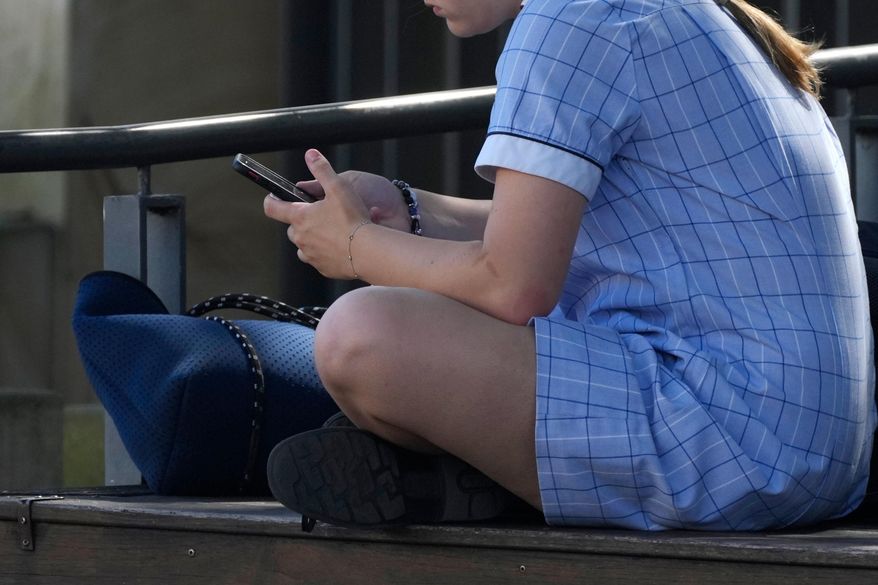 A young girl uses her phone while sitting on a bench, Nov. 8, 2024. (AP Photo/Rick Rycroft, File)