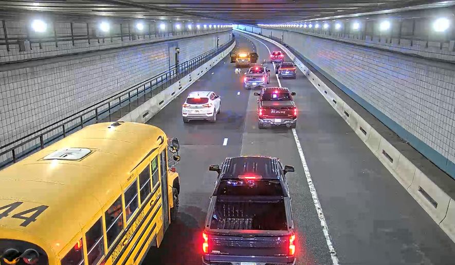 This image from surveillance video shows a Massachusetts state trooper kneeling on the highway and trying to coax a dog to get into his cruiser after the animal run through the Ted Williams Tunnel in Boston during rush hour on Thursday, Nov. 6, 2025. (Massachusetts Department of Transportation via AP)