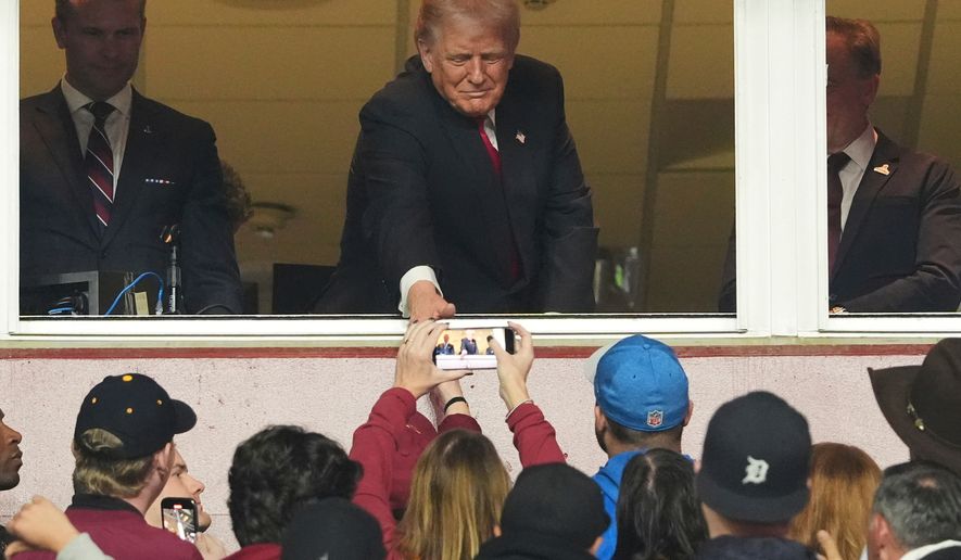 President Donald Trump, center, greets the crowd alongside Defense Secretary Pete Hegseth, left, as they attend an NFL football game between the Washington Commanders and the Detroit Lions at Northwest Stadium in Landover, Md., Sunday, Nov. 9, 2025. (AP Photo/Jacquelyn Martin)