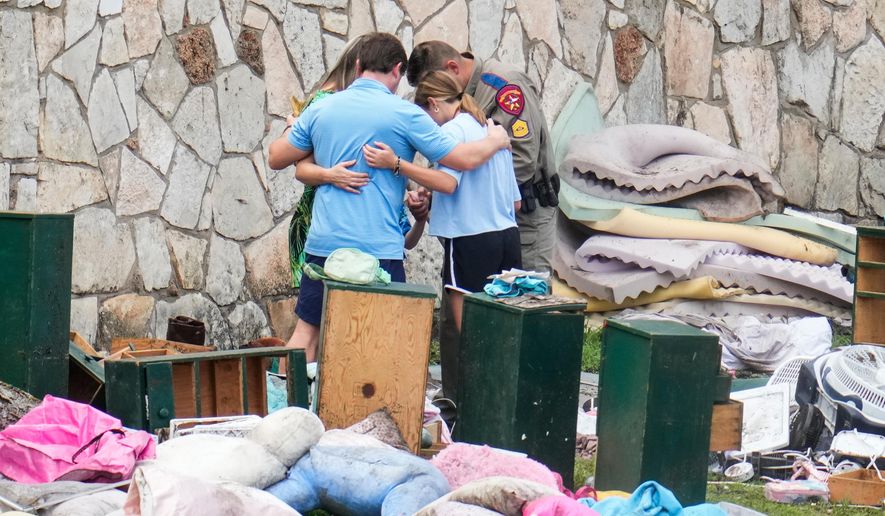 An officer prays with a family as they pick up items at Camp Mystic in Hunt, Texas, July 9, 2025. (AP Photo/Ashley Landis, File)