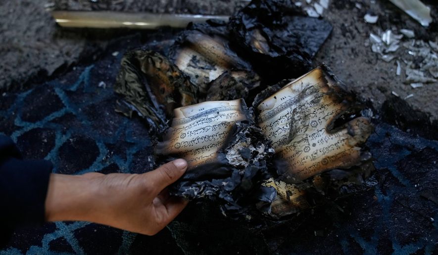 A boy inspects burnt copies of Quran inside a mosque that was torched and defaced by Israeli settlers overnight, in the West Bank town of Deir Istiya Thursday, Nov. 13, 2025. (AP Photo/Nasser Nasser)